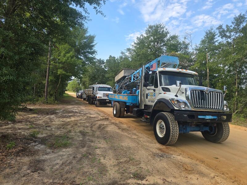 Pollock Well Drilling trucks lined up on a sandy county road